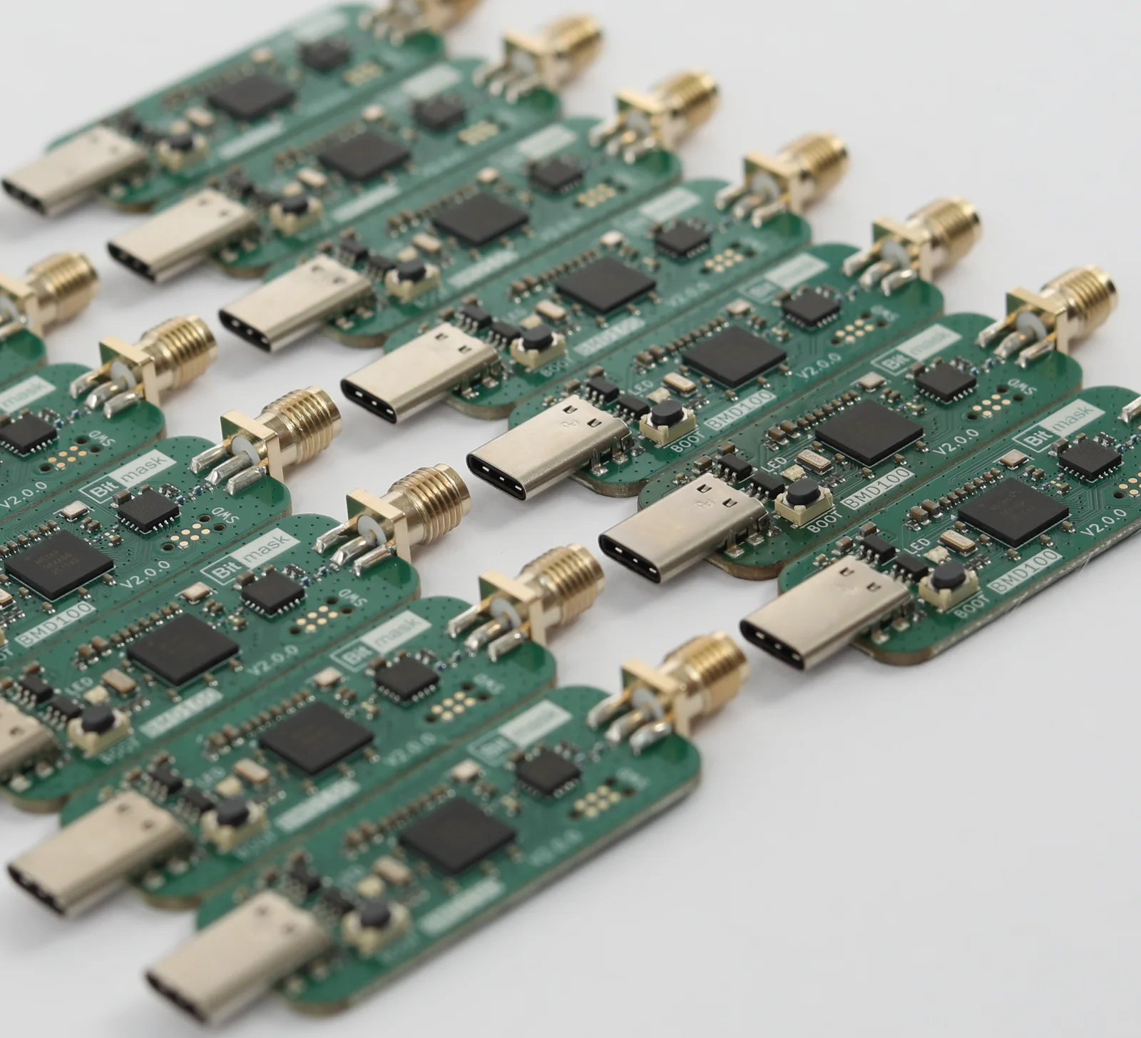 Rows of assembled Bitmask BMD100 v2.0.0 dongles on a white bench, their gold SMA antenna connectors catching the light