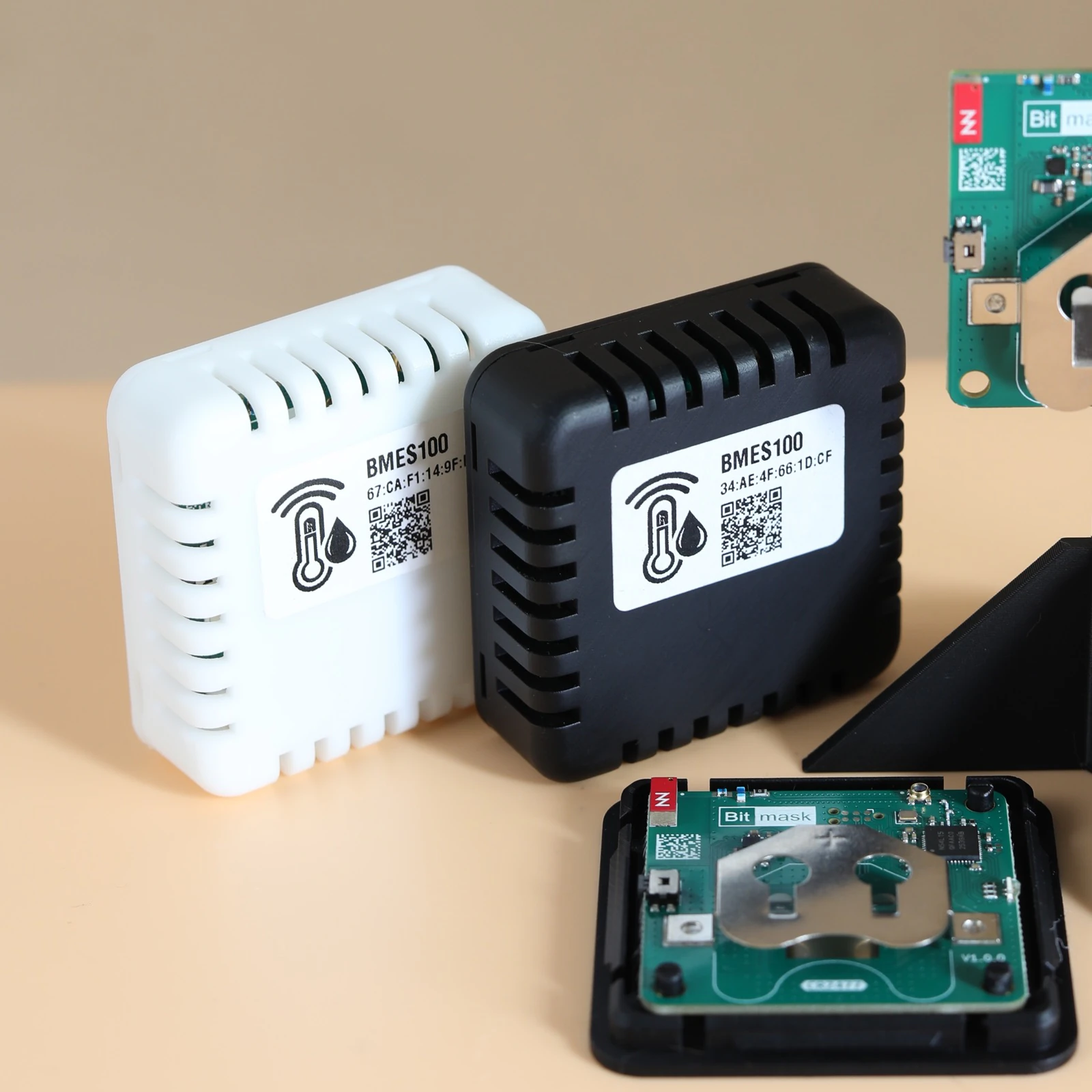 Close-up of white and black BMES100 sensors beside a disassembled unit showing the internal board and coin-cell battery holder