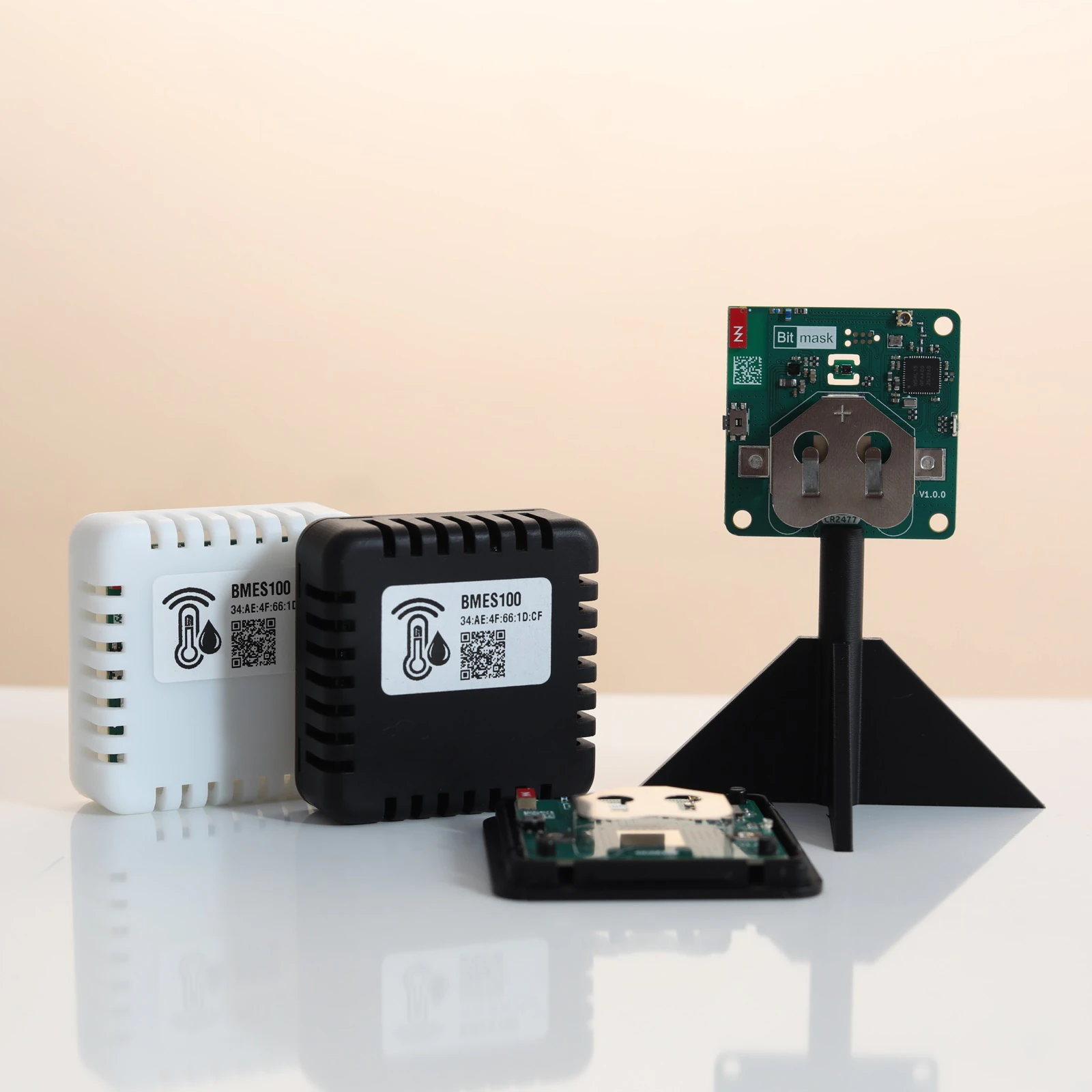 BMES100 sensors in white and black cases next to a bare board on a stand, with a disassembled unit in the foreground